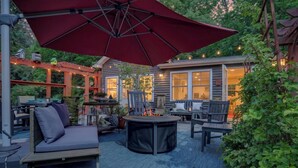 Een terras met een ronde tafel, een bank en een pergola met lichtslingers.