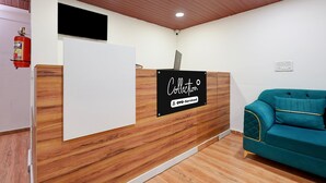 A reception desk with a sign, a teal sofa, wooden flooring, and a ceiling with recessed lighting. - Classic Yuva Inn (Nagpur)