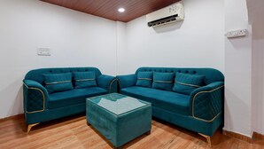 A room with two teal sofas, a glass coffee table, wooden flooring, a white ceiling with recessed lighting, and an air conditioning unit. - Classic Yuva Inn (Nagpur)