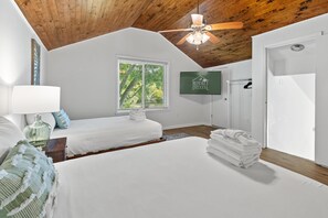 Une chambre avec deux lits, un ventilateur de plafond, une fenêtre avec des stores, une pile de serviettes et un panneau indiquant « ROYAL STAYS ».