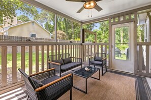Une terrasse couverte, aménagée avec du mobilier d’extérieur et dotée d’un ventilateur de plafond, d’où l’on peut admirer une maison au loin.