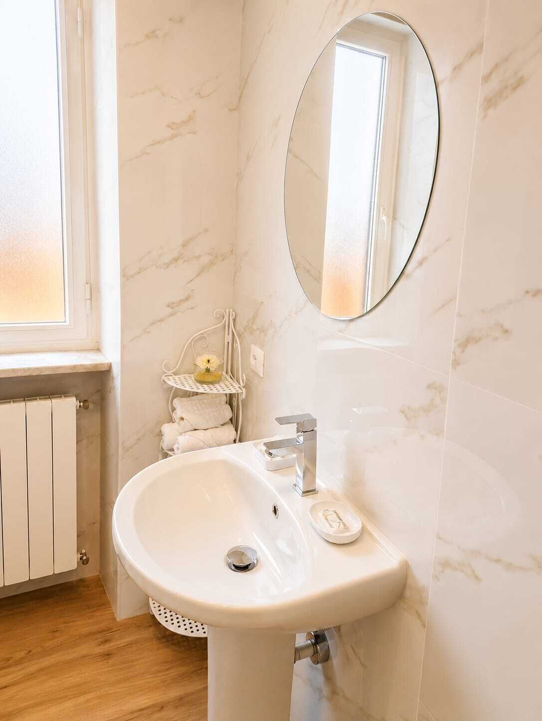 A bathroom with a white marble sink, a round mirror, and a window with a view.