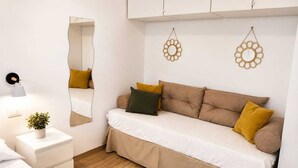 Een moderne slaapkamer met een slaapbank, nachtkastjes, een spiegel en decoratieve wanddecoraties.