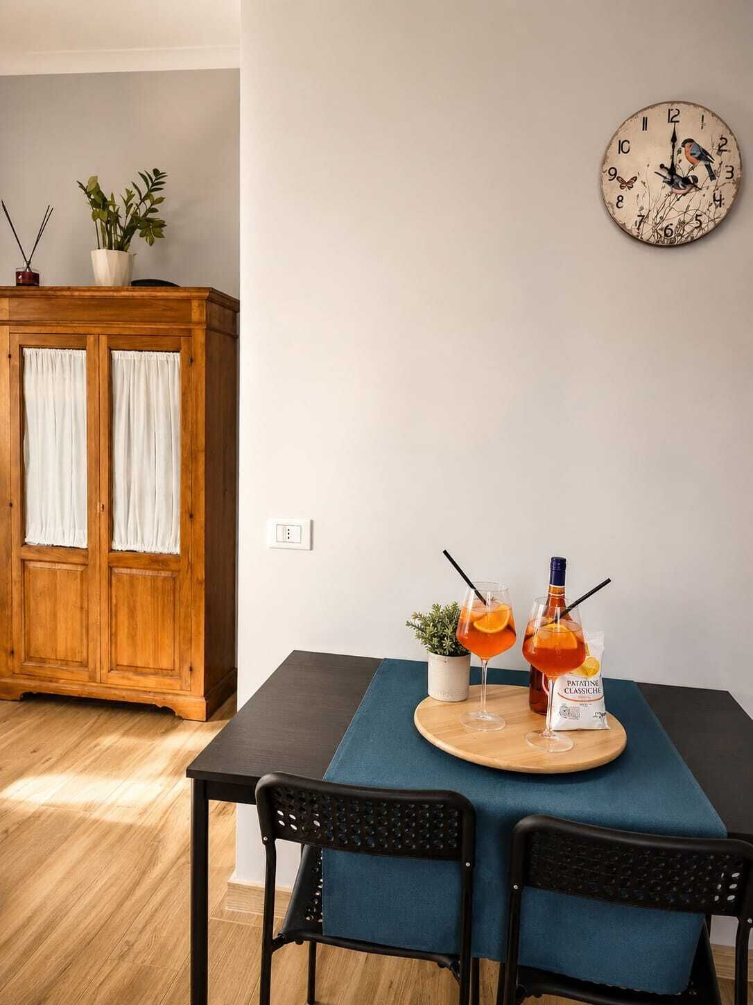 A dining area with a wooden cabinet, a clock, and a table set with a bottle and glasses.