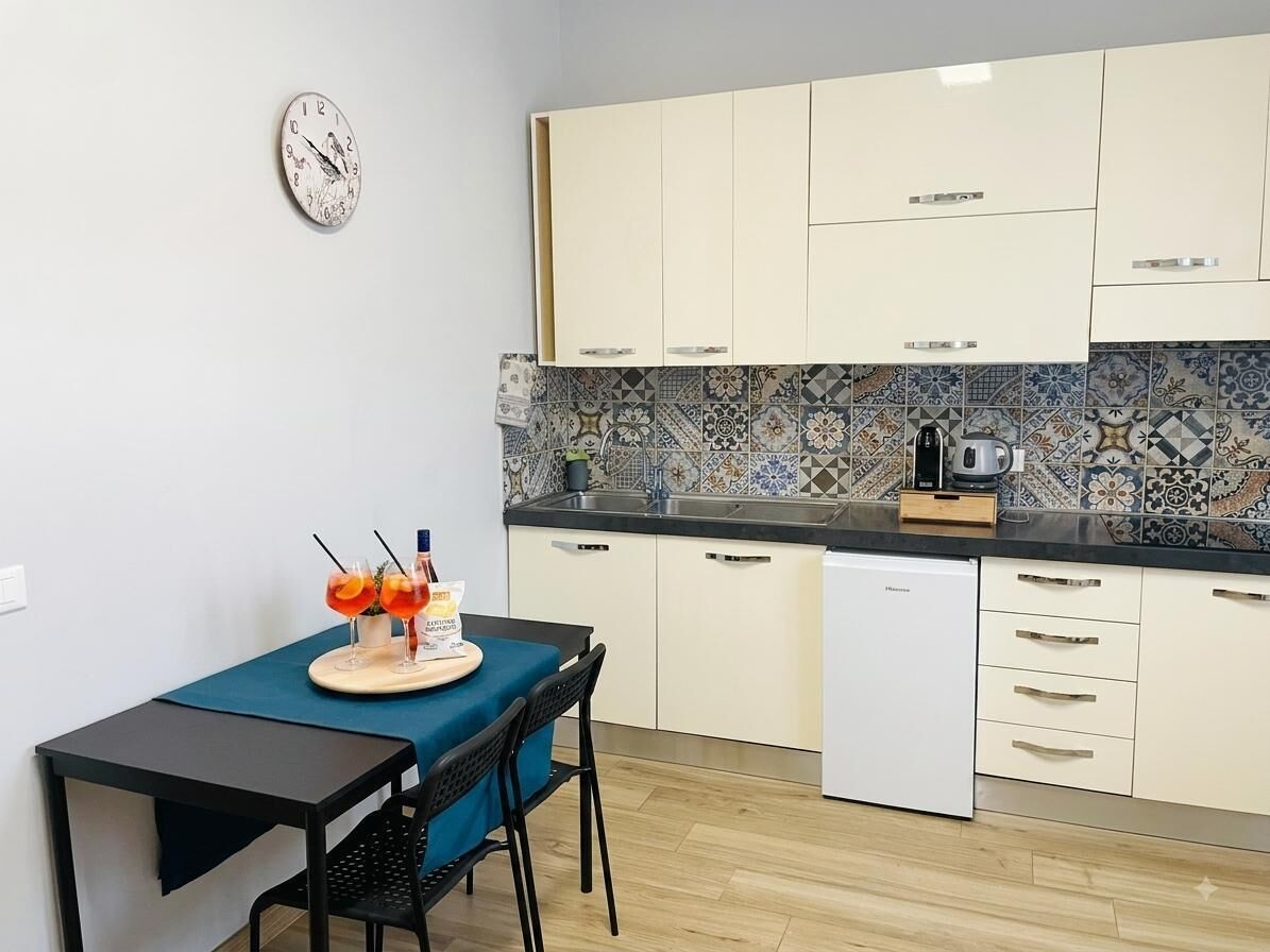 A compact kitchen with a dining area, featuring a clock, a coffee maker, and a small table with chairs.