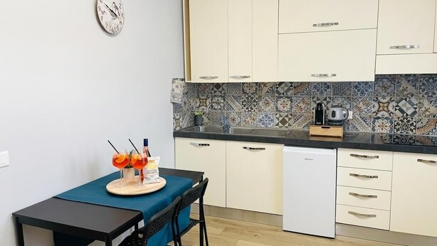 Een kleine keuken met eethoek, voorzien van een klok, koffiezetapparaat en een tafeltje met stoelen.