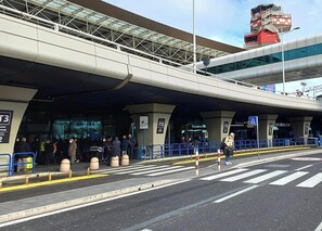Terminal de aeropuerto con pasarela techada, carros de equipaje y paso de peatones.