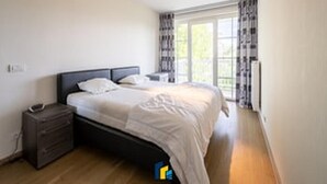 A bedroom with a bed, bedside table, and a window with curtains.