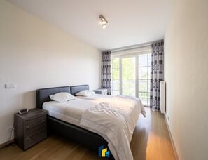 Ein Schlafzimmer mit einem Bett, Nachttisch und einem Fenster mit Vorh ängen.