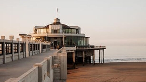 A coastal building with a prominent tower, a walkway leading to it, and a view of the sea.