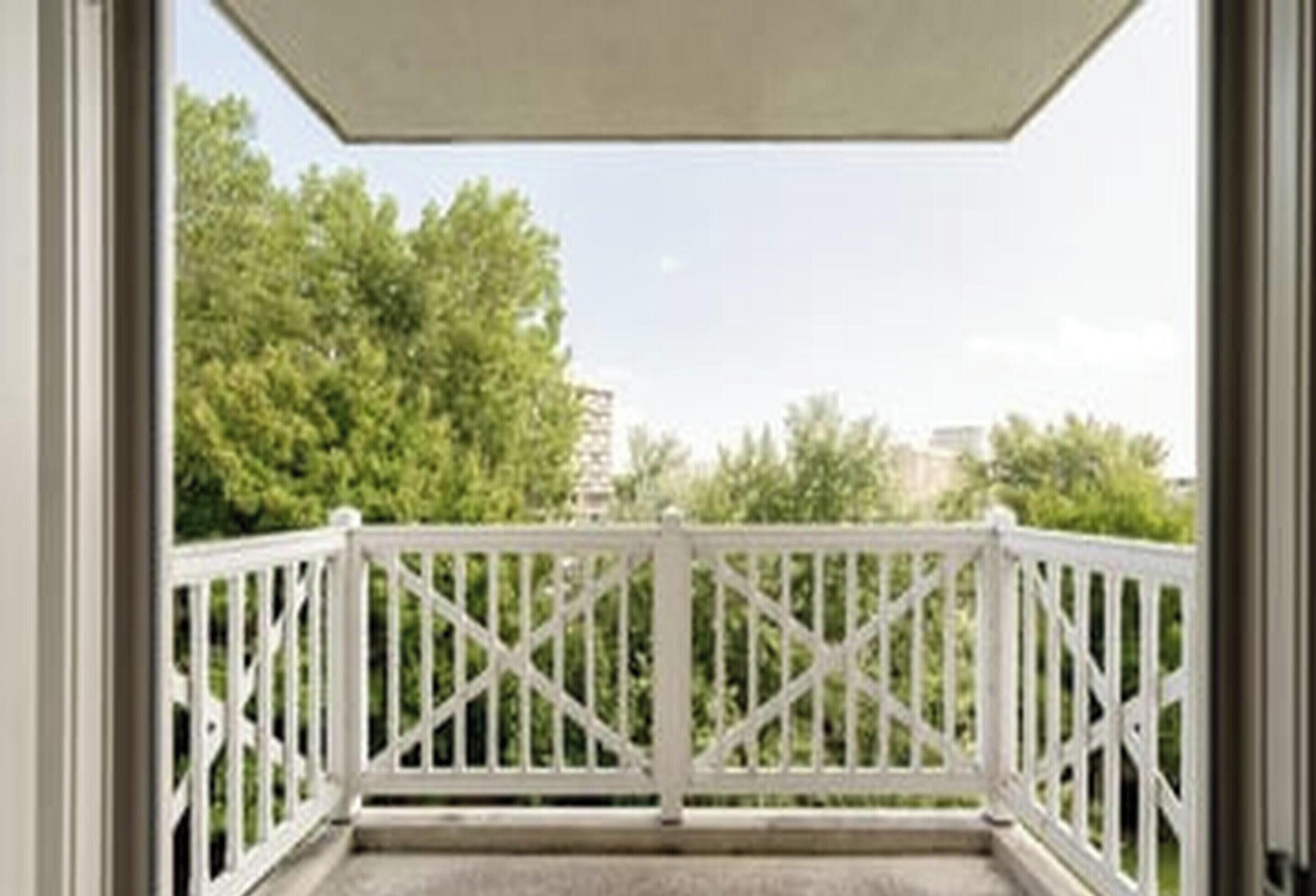A balcony with white railings and a view of trees and buildings.