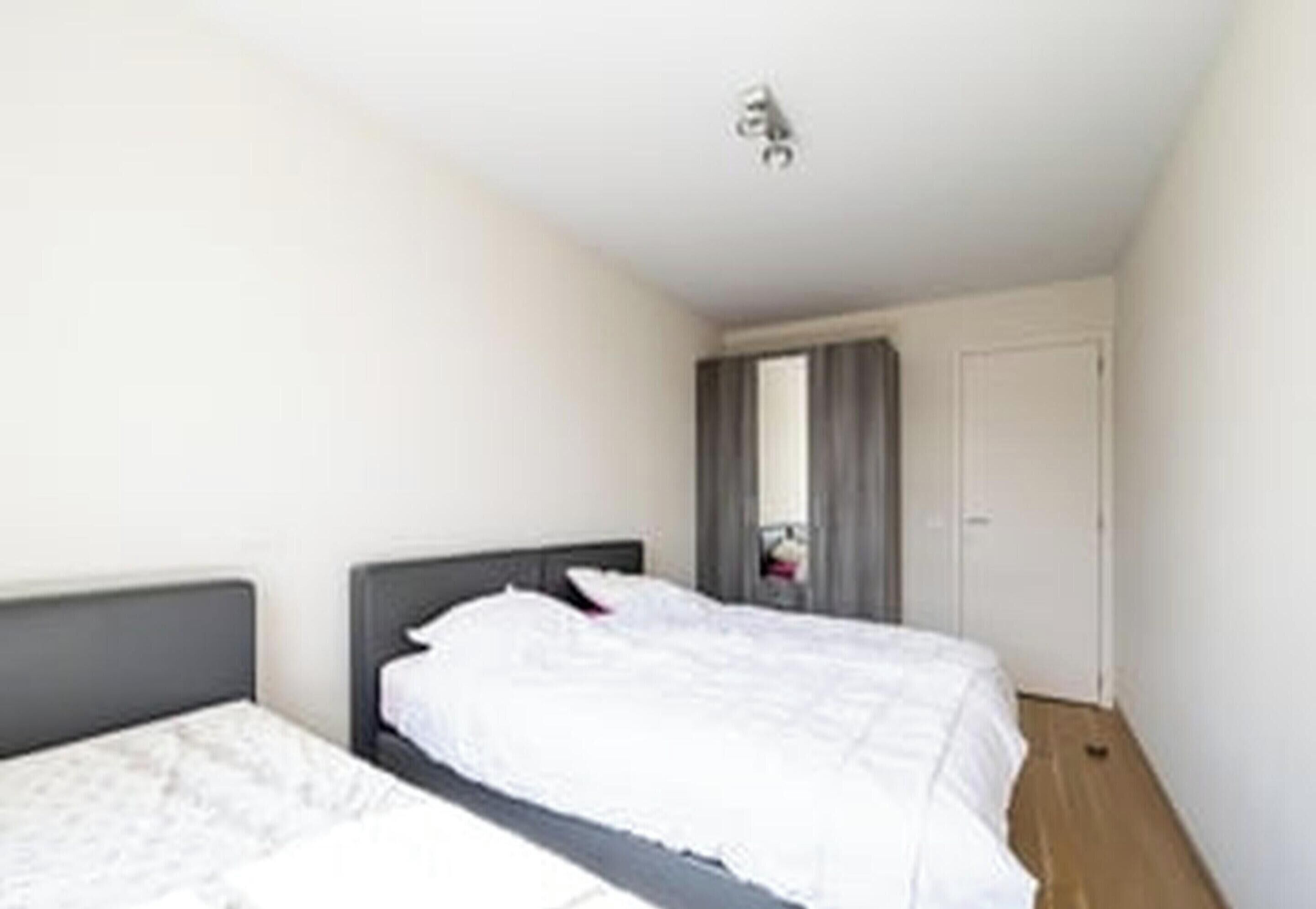 A single bed with a grey headboard, white bedding, and a small bedside table.