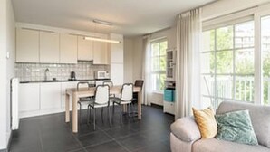 A modern kitchen with white cabinets, a dining area with a table and chairs, and a living area with a sofa and a window.