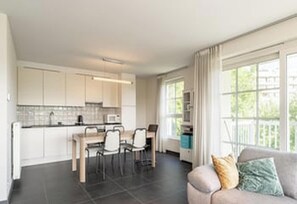 Eine moderne Küche mit weißen Schränken, eine Essecke mit Tisch und Stühlen sowie ein Wohnbereich mit einer Couch und einem Fenster.