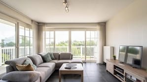 A modern living room with a sofa, coffee table, TV, and large windows.