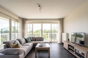 Ein modernes Wohnzimmer mit Sofa, Couchtisch, Fernseher und großen Fenstern.