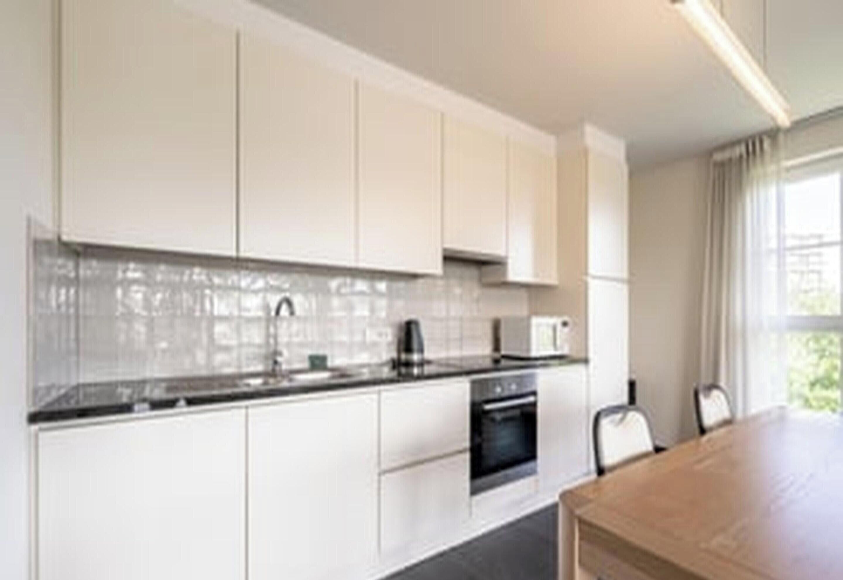A modern kitchen with white cabinets, a black countertop, and a built-in oven.