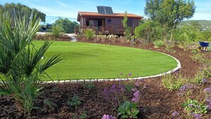 A house with a well-maintained lawn and garden beds with purple flowers. - Peaceful Nature Cabin | 2 Bedrooms | Quinta do Lago & Vilamoura Area | Algarve (Loulé)