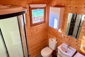 Baño de cabaña de madera con inodoro, lavamanos y ventana con vista a una terraza.