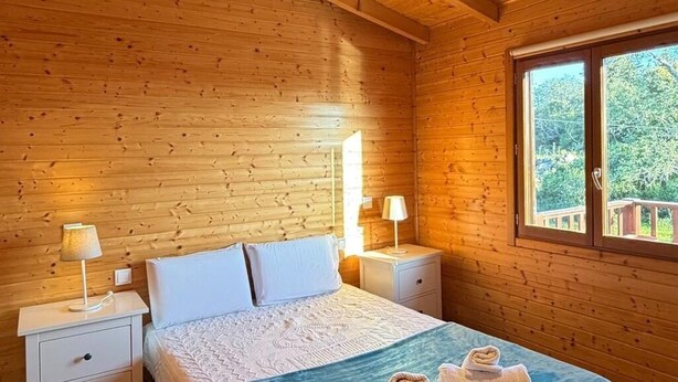 A wooden cabin bedroom with a bed, two bedside tables, and a window. - Peaceful Nature Cabin | 2 Bedrooms | Quinta do Lago & Vilamoura Area | Algarve (Loulé)