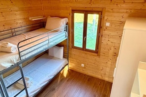 A bunk bed room with a window, wooden walls, and a white cabinet.