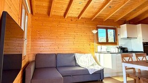 A cozy cabin interior with a sofa, a dining table, and a kitchen area. - Peaceful Nature Cabin | 2 Bedrooms | Quinta do Lago & Vilamoura Area | Algarve (Loulé)