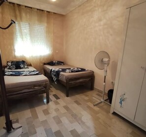 Habitación con dos camas, un armario, un ventilador y una ventana con cortinas.