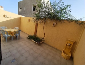 Une petite terrasse extérieure avec une table et des chaises, un pot de fleurs et des toilettes jaunes.