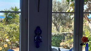 Habitación con vista a un jardín y al mar, una lámpara de pared y un florero con una flor.