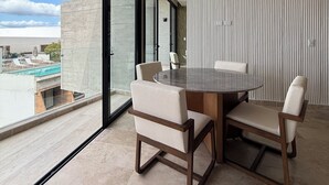 Een moderne eetruimte met een ronde tafel en vier stoelen, grote ramen met uitzicht op een zwembad, en een plafondventilator.