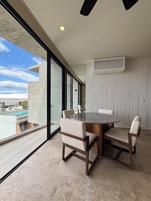 Ein moderner Essbereich mit einem runden Tisch und vier Stühlen, große Fenster mit Blick auf einen Swimmingpool und ein Deckenventilator.