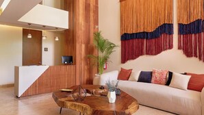 Een receptie met een houten balie, een bank met decoratieve kussens, een bijzettafeltje en een grote plant.