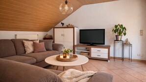 A living room with a sofa, a TV stand, a coffee table, and a plant. - Spacious vacation apartment in a quiet location with lots of nature. Pet friendly! (Tiefenthal)