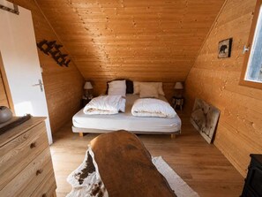 A cozy wooden cabin bedroom with a bed, bedside tables, a dresser, and a window. - The Pyrenees chalet (Arreau)