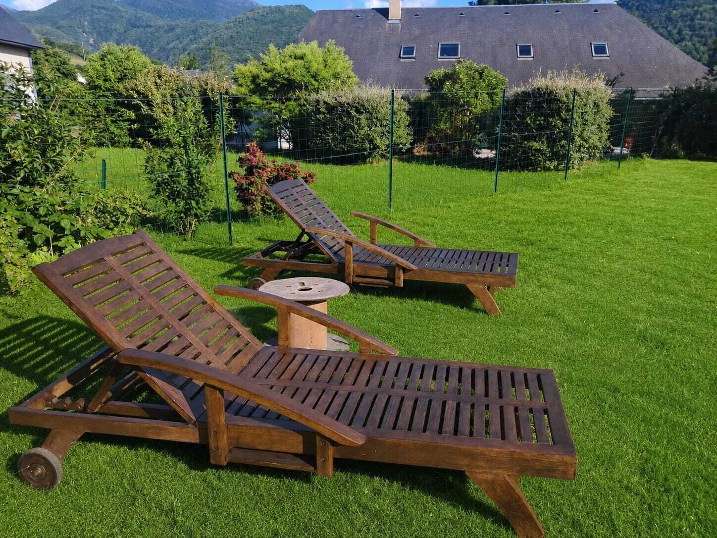 Ein grünes Aussenareal mit zwei Holzliegestühlen und einem kleinen runden Tisch.