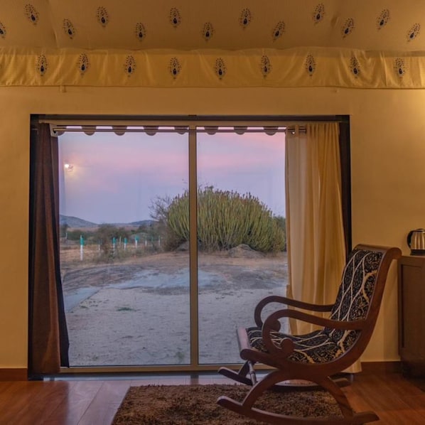 Habitació amb porta corredissa de vidre que dona a un paisatge desert, una cadira de balanc i una taula petita amb un búl.