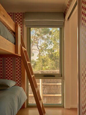 A room with a bunk bed, a window with a view of trees, and a checkered wall pattern. - Lay Day House (Lorne)