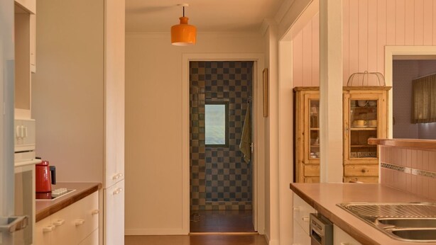 A kitchen with a wooden countertop, a sink, and a hanging orange pendant light. - Lay Day House (Lorne)