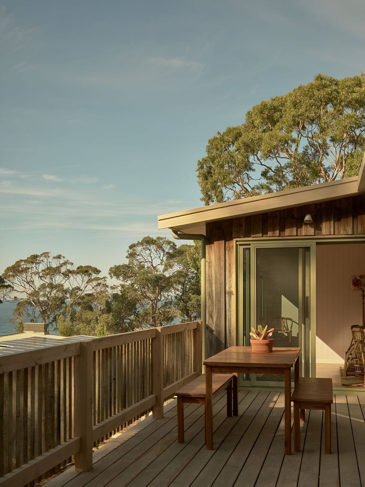 A wooden deck with a table and chairs, overlooking a body of water and trees.