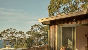 A wooden deck with a table and chairs, overlooking a body of water and trees. - Lay Day House (Lorne)