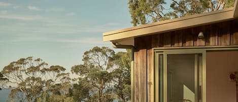 Una terraza de madera con una mesa y sillas, con vistas a un cuerpo de agua y árboles.