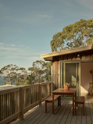 A wooden deck with a table and chairs, overlooking a body of water and trees. - Lay Day House (Lorne)