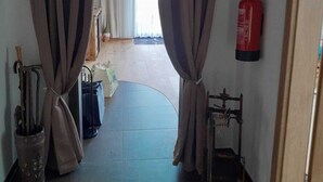 Un pasillo con cortinas, un extintor y una ventana con marco azul.