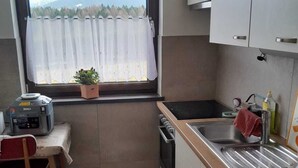 Cocina compacta con ventana, un lavamanos, estufa y una silla.