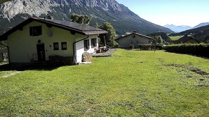 Una casa de campo con techo inclinado, un porche delantero y un pequeño jardín.
