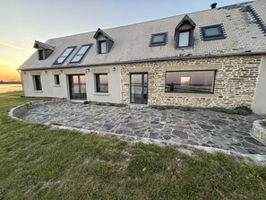 Ein modernes Haus mit Natursteinfassade, zahlreichen Fenstern und einem befestigten Eingangsbereich aus Stein.