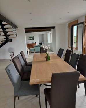 A modern dining area with a wooden table and upholstered chairs, a staircase, and a view of the outdoors. - Gîte La Carelle in Vains at the foot of the Bay of Mont Saint Michel (Vains)