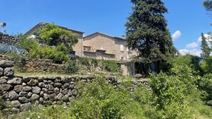 A stone building with a sloped roof, surrounded by greenery and a stone wall.