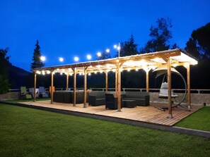 An outdoor covered patio with seating and a grill area, surrounded by a well-maintained lawn.