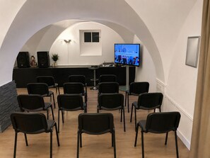 Sala de conferências com teto curvo, tela de televisão, pódio e fileiras de cadeiras.